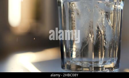 Nahaufnahme des Wassereingießens in das Glas mit Eis auf unscharfem Hintergrund. Klares Wasser mit Eisstücken in ein leeres transparentes Glas geben. Stockfoto