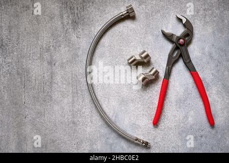 Verstellbare Zangen, Rohrleitungsexzentrische und flexibler Verbindungsschlauch auf grauem Beton-Hintergrund Nahaufnahme Stockfoto