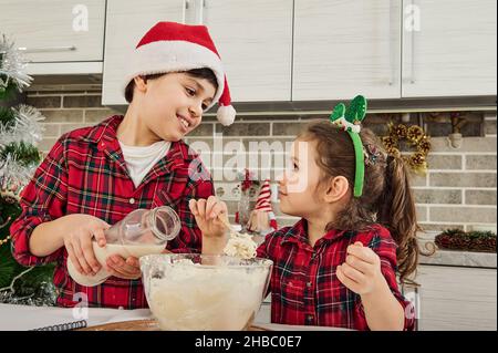 Liebenswerte europäische Kinder genießen die Zeit zusammen, haben Spaß beim Kneten von Teig, Kochen von Cookies und Bäckereien, helfen ihrer Mutter in der Küche zu Hause Stockfoto