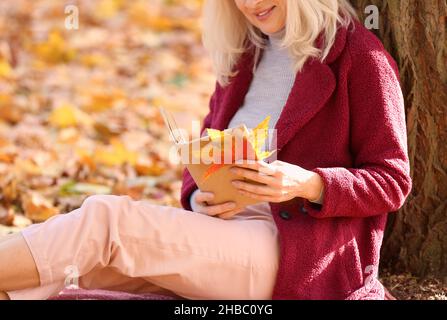 Reife Frau liest Buch im Herbstpark Stockfoto