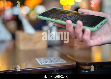 Nahaufnahme der Gäste, die eine Mahlzeit im Restaurant bestellen, während der QR-Code mit dem Mobiltelefon gescannt wird, um ein Online-Menü zu erhalten. Stockfoto