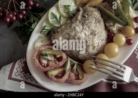 Auf dem Tisch auf einer Leinenserviette steht ein Teller mit gebackenen Hühnerschenkeln und Gemüse. In der Nähe Früchte, Gewürze. Draufsicht, Nahaufnahme. Stockfoto