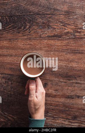 Draufsicht auf anonymen Mann mit Tasse heißen Kaffee mit Milch auf Holztisch platziert Stockfoto