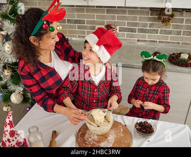 Blick von oben auf die glückliche kaukasische Familie, die in rot-grün karierten Kleidern gekleidet ist und gemeinsam in der Küche Weihnachtsbrot kocht. Schöner, fröhlicher bo Stockfoto