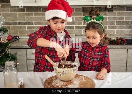Schöne kaukasische Kinder, entzückende Kleinkinder bereiten Weihnachtsbrot zu und gießen Rosinen in eine Schüssel Teig. Bruder und Schwester haben Spaß zusammen Stockfoto