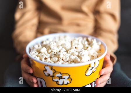Von oben der Ernte unkenntlich Person sitzt auf dem Sofa mit Eimer voll von leckeren Popcorn Stockfoto