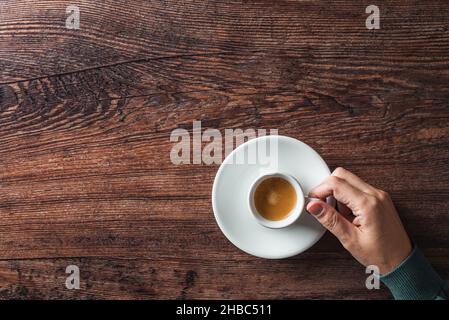 Ansicht von oben auf dem Holztisch mit einer gesichtslosen männlichen Erntegut und einer weißen Tasse heißem Espresso auf einer Untertasse Stockfoto