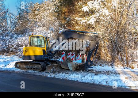 Bagger arbeitet im Winter, um die Straße zu reparieren. Bagger für Erdarbeiten und Straßenbau auf dem Land in der Tschechischen Republik. Straßenreparatur. Stockfoto