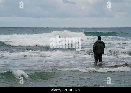 Ein einstehender Fischer, der an einem stürmischen Wintertag knietief im Meerwasser steht. Stockfoto