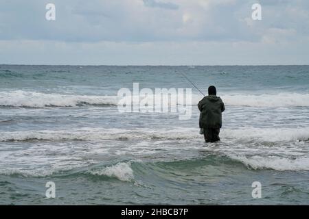 Ein einstehender Fischer, der an einem stürmischen Wintertag knietief im Meerwasser steht. Stockfoto