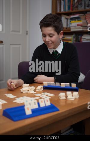 Ein Junge, der Rummikub spielt und eine Kachel legt Stockfoto