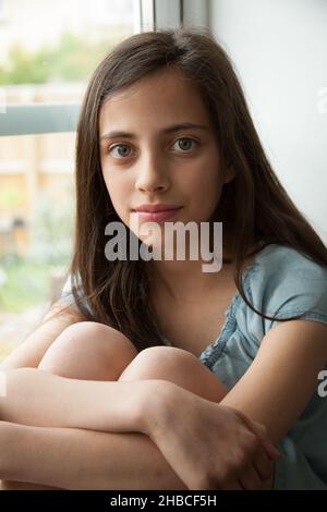 Ein Porträt eines schönen zehnjährigen Mädchens saß auf einer Fensterbank Stockfoto