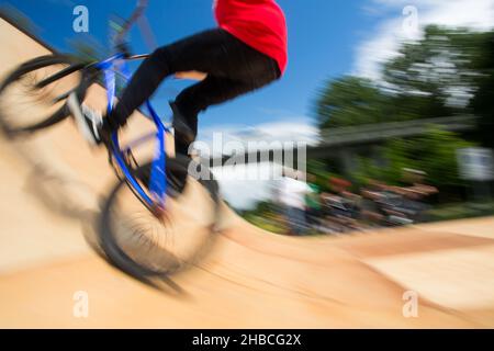 BMX-Fahrer springt auf einer U-Rampe in einem Skatepark über (Bewegungsunschärfe) Stockfoto