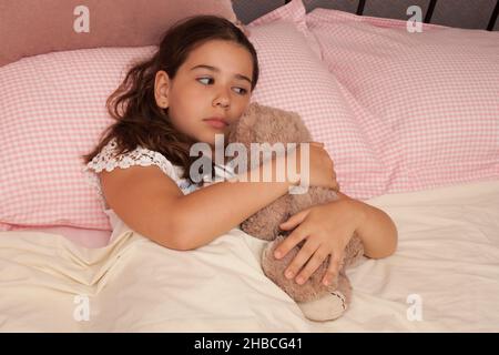 Ein Mädchen in ihrem Bett, das traurig mit ihrem Teddybären kuschelt, aufgenommen am 13. August in Wool, Dorset, Großbritannien Stockfoto