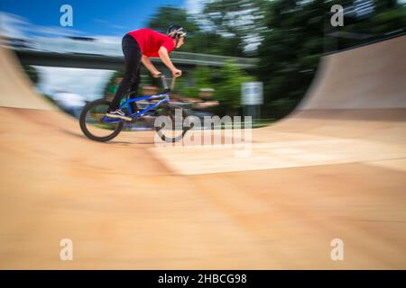 BMX-Fahrer springt auf einer U-Rampe in einem Skatepark über (Bewegungsunschärfe) Stockfoto