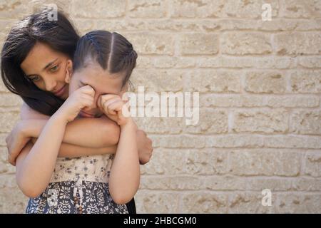 Ein älteres Mädchen unterstützt ein junges Mädchen, das weint Stockfoto