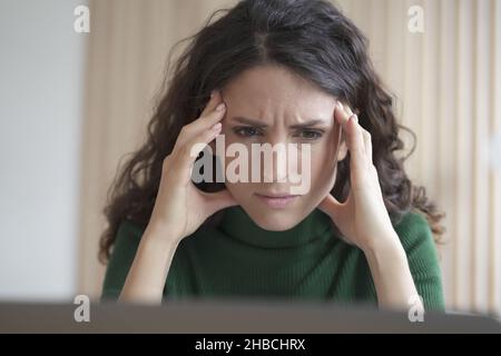 Besorgte junge italienische Mitarbeiterin, die mit frustrierter Gesichtsausdruck auf den Computerbildschirm schaut Stockfoto