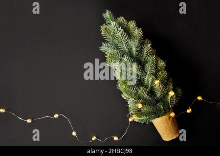 Vorbereitung von Dekorationen für Winterfeste. Künstlicher Weihnachtsbaum, natürlicher Jutefaserstreifen, dunkler Hintergrund, gemütliche Beleuchtung Stockfoto