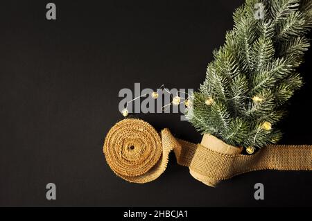 Vorbereitung von Dekorationen für Winterfeste. Künstlicher Weihnachtsbaum, natürlicher Jute-Faserstreifen, dunkler Hintergrund, gemütliche Beleuchtung. Weihnachten moo Stockfoto