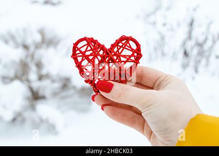 Die Hand hält ein rotes Herz aus Holz aus Zweigen. Umweltfreundlicher Valentinstag. Handgemachtes Geschenk. Symbol der Fürsorge für die Natur. Stockfoto