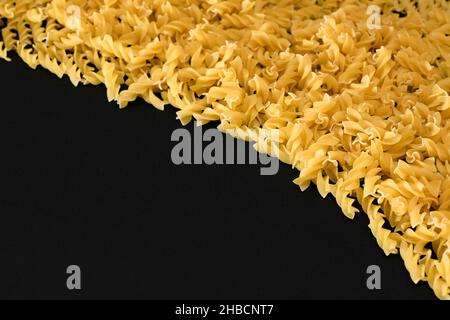 Ungekochte Fusilli-Pasta mit Copy Space auf schwarzem Hintergrund. Rohe und trockene Macaroni. Fett und ungesunde Lebensmittel - Flat Lay Stockfoto