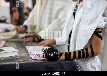 Nahaufnahme, junge Männer lesen jüdisches Gebet und eine Hand mit Tefillin und Talit.Selektiver Fokus Stockfoto