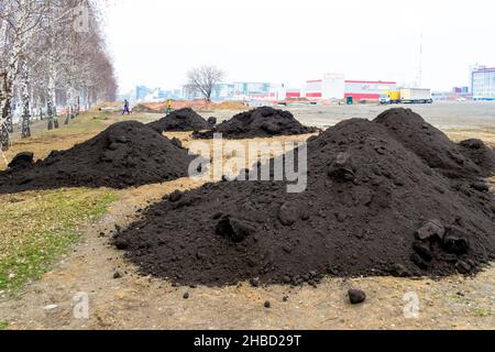 Haufen von schwarzem Boden oder schwarzem Boden wurden auf Lehm gegossen, um Rasen und Blumenbeete zu arrangieren, sowie um Bäume im Prozess des Implement zu Pflanzen Stockfoto