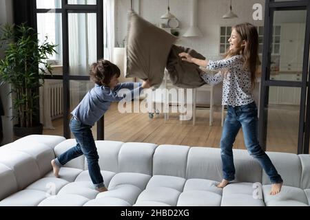 Überglücklich kleine Schwester und Bruder Kissen kämpfen, springen auf Couch Stockfoto