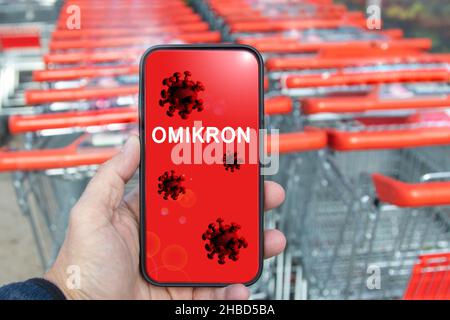 Display eines Mobiltelefons, Einkaufstrolleys im Hintergrund. Display zeigt covid-19 Virus und das Wort omikron Stockfoto