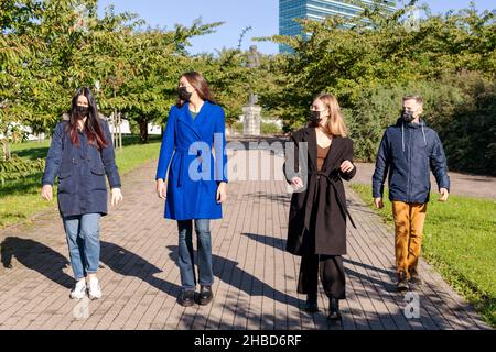 Neu ist normal, Gesundheitswesen, covid-19 Konzept. Vier Freunde mit schwarzen Medikamenten Gesichtsmasken, die an sonnigen und warmen Tagen in sicherer Entfernung im Park spazieren Stockfoto