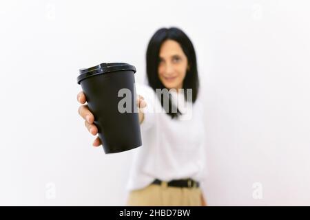 Glückliche kaukasische Frau in smarter Kleidung zeigt schwarzen Einweg-Kaffee-Pappbecher in weißem Hintergrund isoliert schließen. Concep von Werbung und Kaffee-Indu Stockfoto