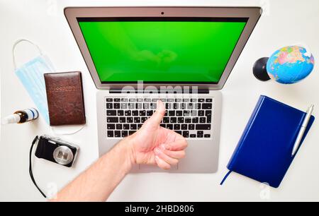 Desktop-Computer mit grünem Bildschirm, blauem Notebook, Kugelständer, Reisepass, Kompaktkamera und Hand zeigen Daumen nach oben auf weißem Hintergrund. Reisen internatio Stockfoto