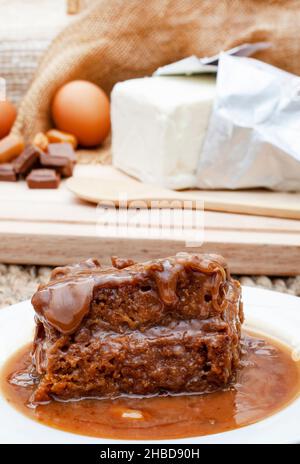 Sticky Toffee Pudding serviert mit selektivem Fokus und Zutaten im Hintergrund Stockfoto