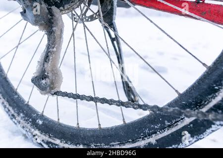 Nahaufnahme von gefrorenem Fahrradwerfer und Kette mit eisigen Schnee im Hintergrund. Radfahren bei extremen Winterbedingungen. Stockfoto