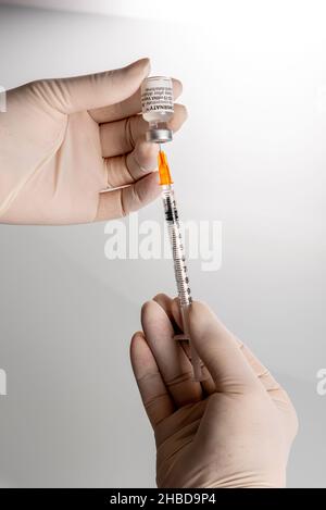 Turin, Italien - 18. Dezember 2021: Pfizer-BioNTech COVID-19-Impfstoff Fläschchen, Krankenschwesternhände mit Latexhandschuh, die eine Dosis Impfstoff aufnehmen Stockfoto