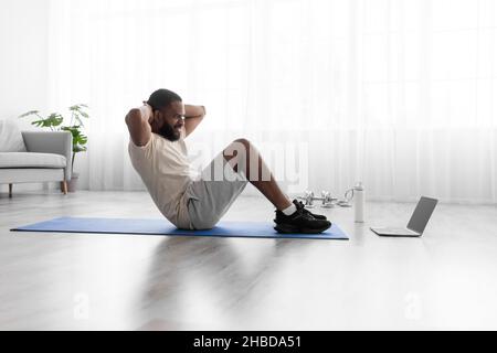 Lächelnder junger schwarzbärtiger Athlet in weißen Sportkleidung macht Bauchübungen Stockfoto