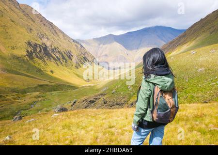 Die Backpacker-Frau steht auf dem Felsen und genießt einen atemberaubenden Blick auf die Berge im Juta-Tal. Erkundung des Nationalparks Kazbegi Stockfoto