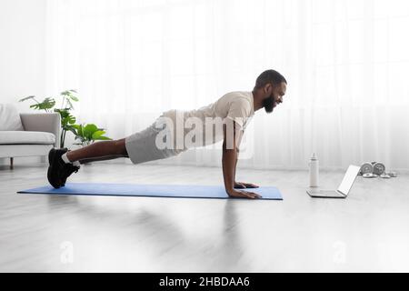 Froher junger schwarzbärtiger Athlet in weißer Sportform macht Push-up, Plank Stockfoto