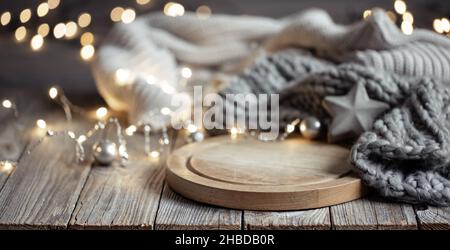 Gemütlicher Hintergrund mit gestricktem Element auf einem Holzelement und Bokeh-Lichtern. Stockfoto