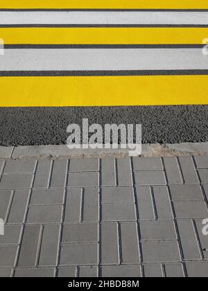 Frisch lackierter Fußgängerübergang mit gelben und weißen Markierungen auf Asphalt, vertikales Foto, Sonnenlicht Stockfoto