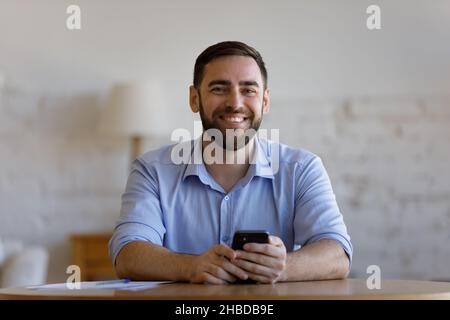Porträt eines lächelnden jungen, gutaussehenden Geschäftsmannes, der sein Mobiltelefon hält. Stockfoto