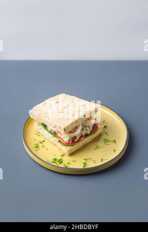 Gesundes Thunfisch-Sandwich mit Eiern Tomate und Salat in gelber Platte auf grauen Trendfarben Stockfoto