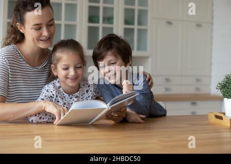 Liebevolle kaukasische Mutter mit Kindern, die zu Hause Buch lesen Stockfoto