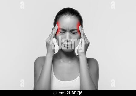 Asiatische Frau, die unter Kopfschmerzen leidet und ihre Tempel berührt Stockfoto