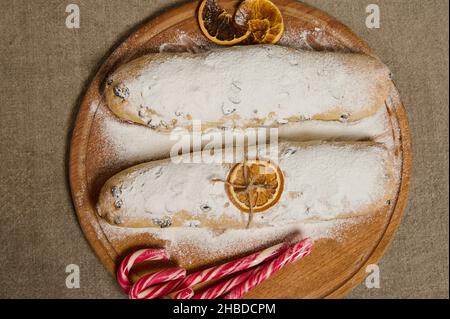 Flache Lebensmittelzusammensetzung. Ansicht des traditionellen deutschen Brotstollens, der zu Weihnachten gebacken wurde, verziert mit einer trockenen Orangenscheibe und einem Seil, Süßigkeiten Ca Stockfoto