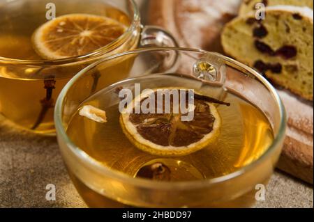 Speisen und Getränke im Hintergrund. Nahaufnahme von Glasküssen mit Kräutertee mit getrockneten Orangenscheiben und Nelken auf dem Hintergrund von geschnittenem hausgemachtem traditionellem Ge Stockfoto