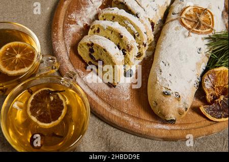 Blick von oben auf frisch gebackenes traditionelles deutsches Stollenbrot, bestreut mit Puderzucker, verziert mit einem Seil und getrockneter Orangenscheibe auf einem Holzschwein Stockfoto
