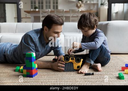 Kleiner Sohn repariert Spielzeugauto mit liebendem Vater, mit Schraubendreher Stockfoto