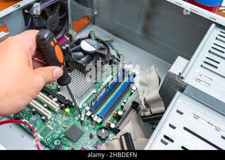 Computerreparaturmann bei der Arbeit, Schrauben Sie die Schrauben mit einem Schraubendreher von der Hauptplatine ab Stockfoto