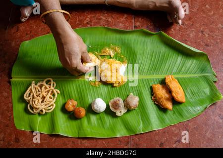 Frau, die am Tag des indischen Festes traditionelles Essen auf Bananenblatt isst. Stockfoto